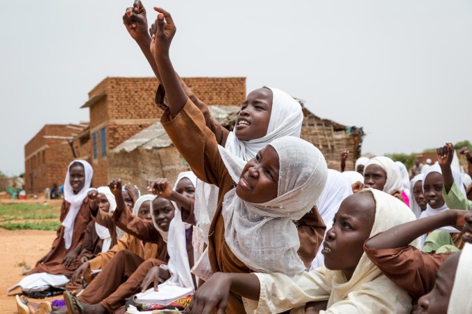 Students try to get the teacher's attention to answer a question. The girls are sitting outside in the sweltering heat because their classroom--made of bamboo--fell down during a storm. Nurul Islam Basic School for Girls, Nyala South Locality, South Darfur, Sudan